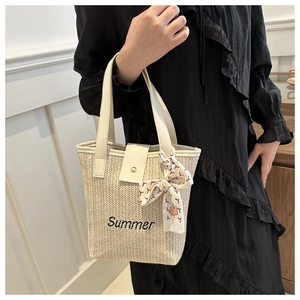 Close-up of summer woven straw bag with black embroidery and decorative silk scarf