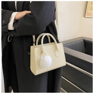 Detail of off-white chevron quilted handbag with round handle and plush ball charm