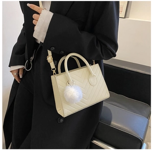 Mini borsa a tracolla trapuntata color crema con pompon in peluche indossata da modella