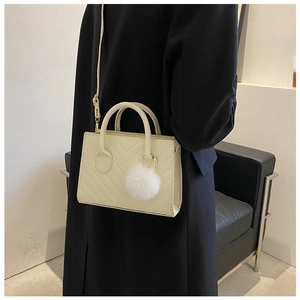 Detail of cream chevron quilted handbag with plush charm shown on a female model