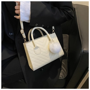 Detail of a white quilted crossbody bag featuring a plush ball charm on a black blazer