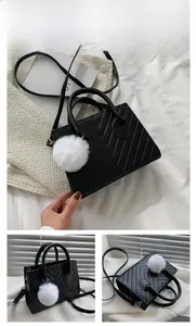 Detail of black quilted shoulder bag with V-shaped texture and faux fur ball accessory