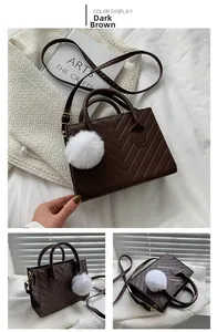 Detail view of dark brown crossbody bag with V-shaped stitching and white plush charm