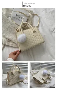 Detail view of cream white crossbody bag with V-quilted pattern and fluffy ball charm