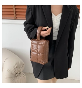 Detail of dark brown quilted puffer handbag with glossy finish held by a model