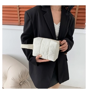 Quilted off-white puffy handbag with hand strap held by model in professional suit