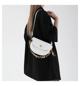 Close-up of white saddle bag with golden clasp and silk scarf wrapped chain strap