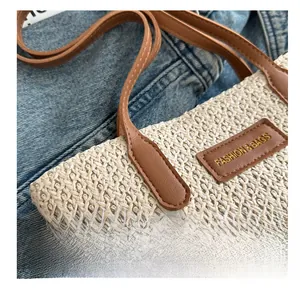 Détail d'un cabas en paille tressée avec bandoulière en cuir brun et logo doré