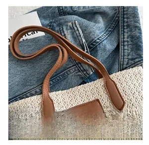 Détail d'un sac cabas en paille avec poignées en cuir marron et écusson logo en relief