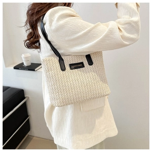 Détail du grand sac cabas en paille avec anses en cuir noir et écusson de mode