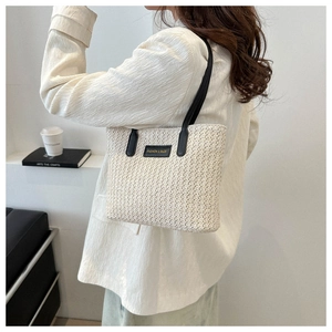 Détail du cabas en paille crème avec poignées en cuir noir et logo de mode élégant