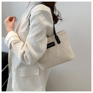 Détail du grand sac cabas en paille avec bandoulières en cuir noir et étiquette fashion