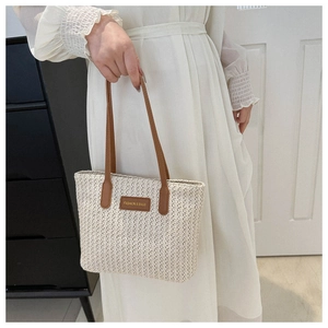 Détail du sac cabas en paille d'été avec bandoulières en cuir et écusson logo décoratif