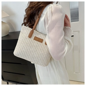 Détail du sac cabas en paille tissée avec anses en cuir marron et écusson logo mode