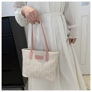 Détail du sac cabas en paille tissée avec anses en cuir rose et écusson de mode