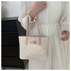 Détail du sac cabas en paille avec bandoulière en cuir rose porté par un mannequin