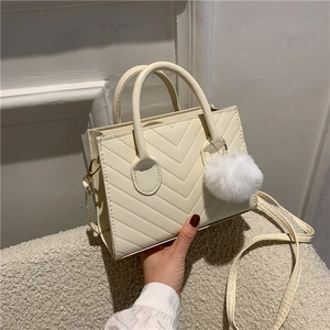 Elegant cream quilted handbag with pompom charm shown in a minimalist setting