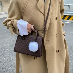 Borsa a tracolla trapuntata marrone con ciondolo a pompon bianco e trench color kaki