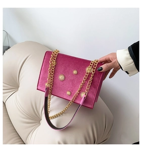 Close-up of fuchsia velvet shoulder bag with golden sunflower accents and chain strap