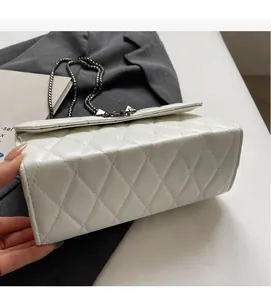 Close-up detail of white quilted leather texture and dark metal chain on the handbag