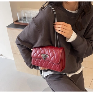 Detail of dark red quilted chain bag with metal clasp worn by a model in casual setting