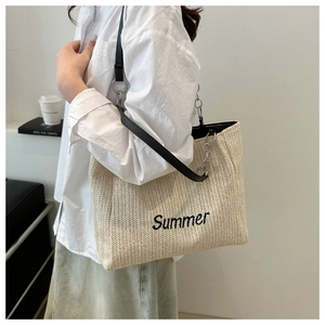 Detail view of woven straw tote bag featuring black Summer embroidery and leather strap