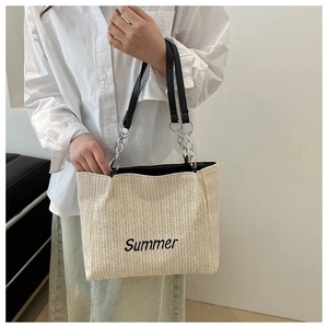 Detail of woven straw tote bag with black Summer embroidery and leather chain handle