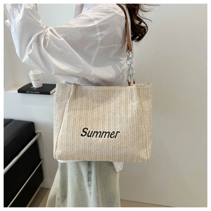 Detail of a white woven straw tote bag with black Summer embroidery and chain strap
