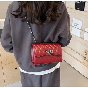 Detail of red quilted crossbody bag with silver chain strap and metal lock closure