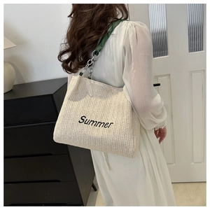 Detail of straw tote bag featuring Summer embroidery and green leather chain strap