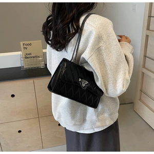 Detail of black quilted leather shoulder bag featuring silver chain and metal lock closure