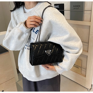 Detail of black quilted leather shoulder bag with metallic chain strap and lock closure