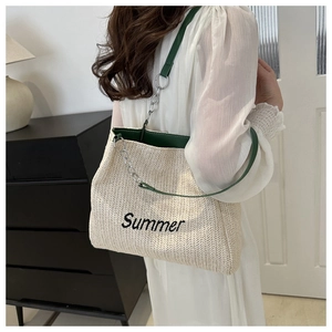 Detail of straw woven tote bag featuring dark green leather trim and Summer embroidery