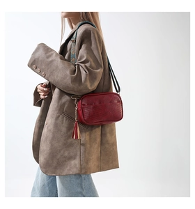 Detail of red leather crossbody bag with ethnic strap and gold tassel accent