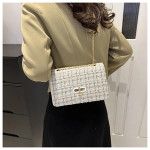Detail of tweed crossbody bag with gold chain strap and turn-lock closure on a model