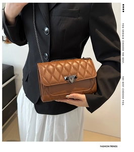 Detail of brown quilted crossbody bag with metal chain strap and rivet buckle closure
