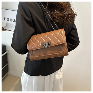 Detailed view of brown quilted crossbody bag with metal lock and chain strap on a model