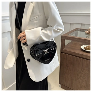 Détail du sac à bandoulière coeur en cuir verni noir avec rivets argentés et boucle métal