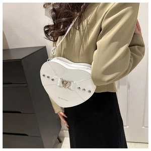 Sac bandoulière blanc en forme de cœur avec rivets porté sur un blazer de couleur kaki