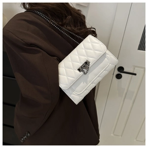 Detail view of white quilted crossbody bag with metal chain strap and turn-lock closure