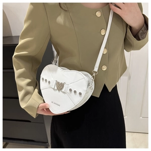 Détail du sac blanc en forme de cœur avec rivets argentés et boucle métallique porté à l'épaule