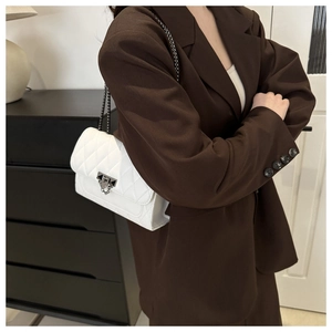 Detail of white quilted crossbody bag with silver metal chain strap and lock closure
