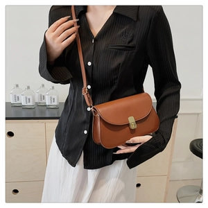 Sac bandoulière en cuir marron avec boucle dorée porté par un mannequin en situation