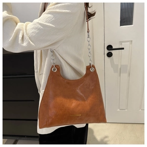 Détail d'un cabas marron vintage avec œillets argentés et chaîne sur un blazer