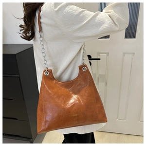 Detail of caramel brown glossy PU leather tote bag featuring a moon crescent shape and chain strap