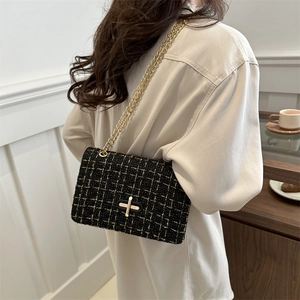 Chic black tweed plaid shoulder bag with gold chain strap worn by a model in a cozy interior