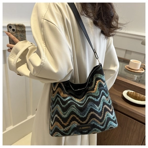 Detail of knit bucket bag with colorful wavy patterns and black leather shoulder strap