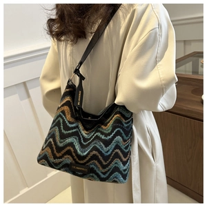 Detail view of woven knit shoulder bag with colorful wave patterns on a beige trench coat