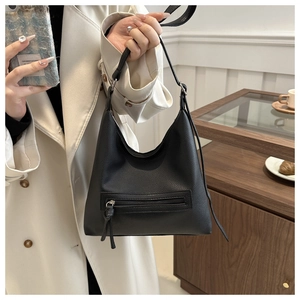 Detail of black lychee texture tote bag featuring a front zipper with long tassels