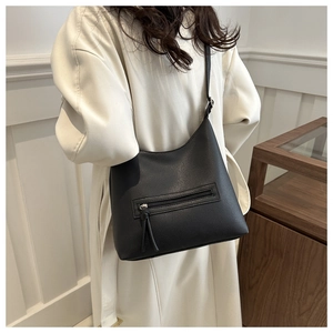 Detail of black pebbled leather tote bag with long tassel zipper on a model shoulder